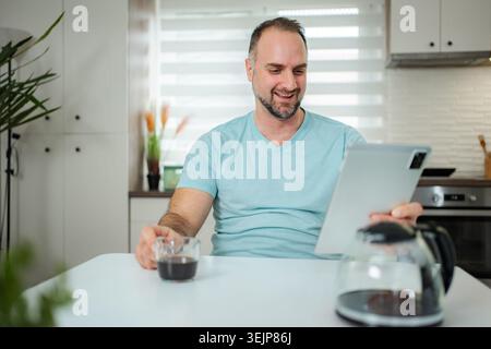Man smiling enjoying coffee while using tablet at home Stock Photo