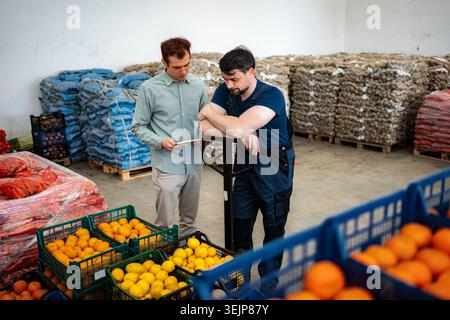 Warehouse manager discussing inventory with worker checking vegetables Stock Photo