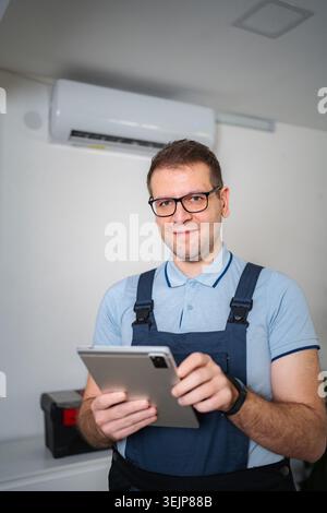 HVAC technician smiling holding digital tablet checking air conditioner Stock Photo