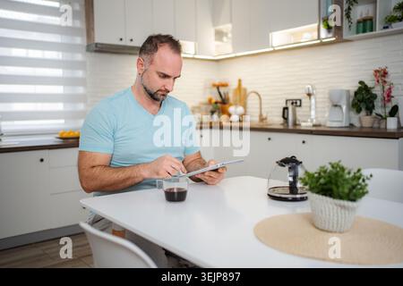 Man drinking coffee and using tablet in kitchen at home Stock Photo