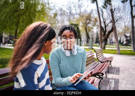 Young adult female friends sharing content on digital tablet in park Stock Photo