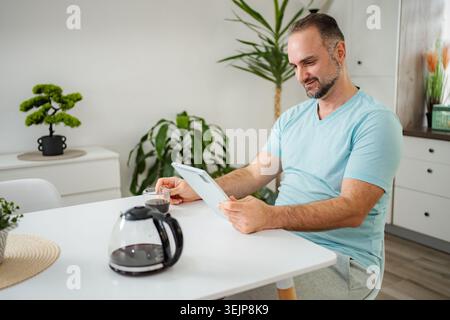 Man drinking coffee and using digital tablet at home Stock Photo