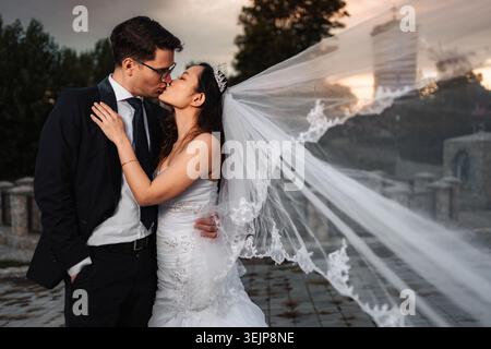 Interracial wedding couple kissing outdoors with flowing veil Stock Photo
