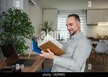 Man smiling reading notebook working from home office Stock Photo