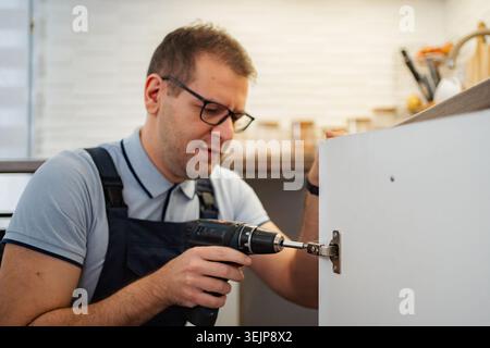 Handyman installing kitchen cabinet door using electric drill Stock Photo