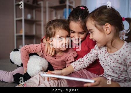 Sisters sharing tablet at home enjoying playtime together Stock Photo