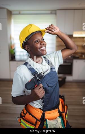 Smiling african american female construction worker holding cordless drill and adjusting hardhat Stock Photo