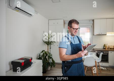 Technician checking air conditioner with digital tablet at home Stock Photo