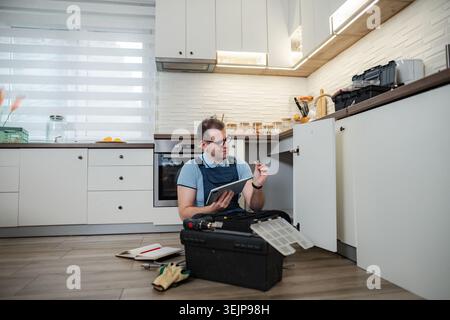 Handyman repairing kitchen cabinet using digital tablet for home improvement Stock Photo