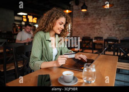 Smiling woman using laptop and credit card, shopping online in a cafe Stock Photo