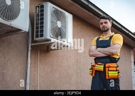 Technician posing with arms crossed in front of air conditioners on a wall Stock Photo