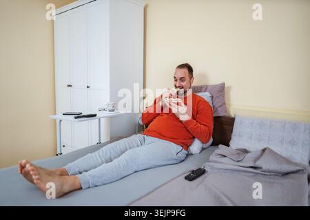 Man enjoying snack cookies in bed relaxing at home Stock Photo