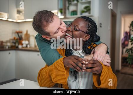 Interracial couple sharing happy intimate moment in kitchen Stock Photo