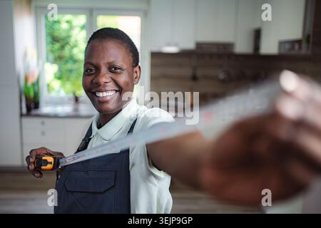 Portrait of a cheerful black female worker using measuring tape in a kitchen Stock Photo