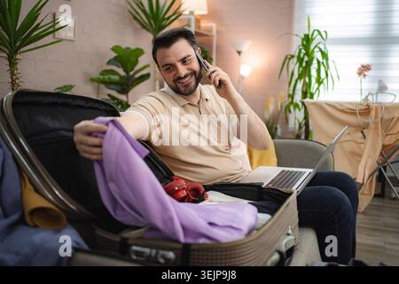 Man packing suitcase while talking on the phone Stock Photo