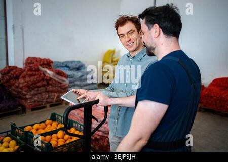 Warehouse manager and worker discussing inventory on digital tablet Stock Photo