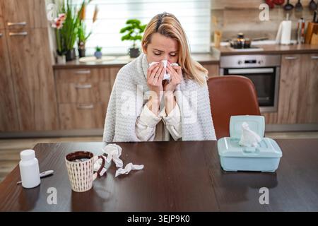 Woman feeling unwell while sitting in a cozy kitchen on a chilly morning Stock Photo