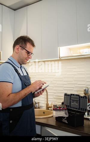 Handyman using tablet near toolbox in modern kitchen Stock Photo
