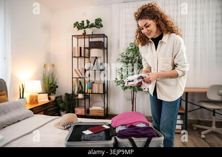 Woman packing suitcase for vacation trip in bedroom Stock Photo