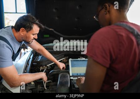 Two mechanics repairing a car engine using a computer diagnostic software Stock Photo