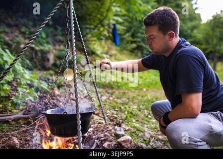 Hiker preparing food on campfire in forest Stock Photo