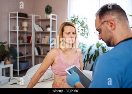 Doctor examining woman with skin rash using digital tablet Stock Photo