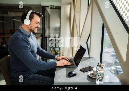 Adult man working remotely on laptop wearing headphones Stock Photo