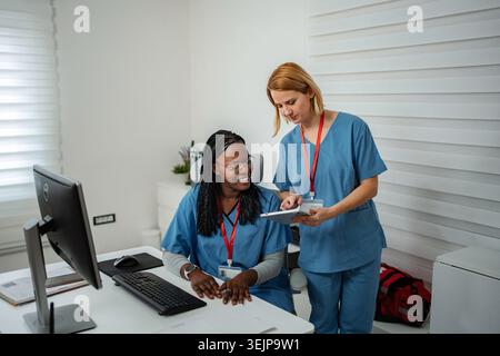 Two nurses discussing patient data on a digital tablet in a clean office setting Stock Photo