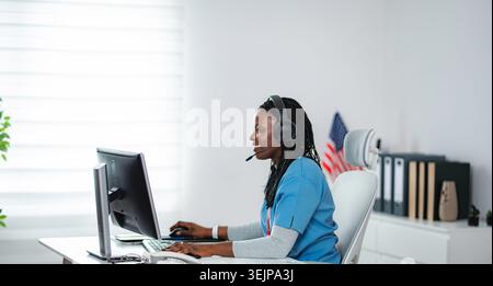 African American medical professional wearing headset working on computer and talking Stock Photo
