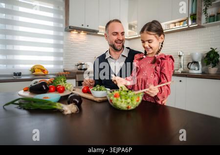 Father and daughter preparing healthy salad together in kitchen Stock Photo