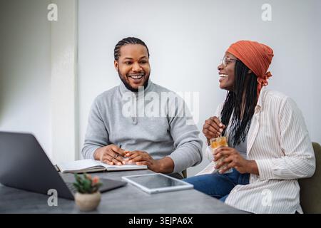 Black coworkers laughing and collaborating over laptop Stock Photo