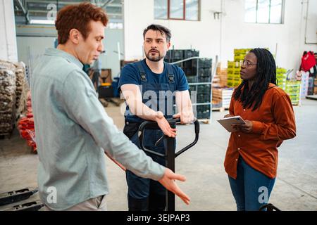 Diverse group of logistics workers having a serious conversation in a warehouse Stock Photo