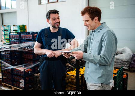 Workers discussing logistics in fresh produce warehouse with tablet Stock Photo
