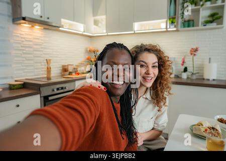 Two smiling diverse women taking selfie in home kitchen Stock Photo