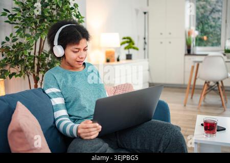 Young woman relaxing at home using laptop with headphones Stock Photo