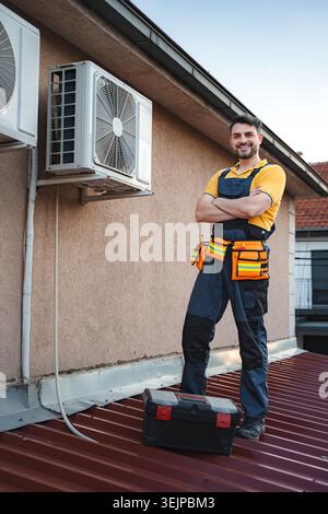Hvac technician posing with arms crossed after installing an air conditioner on a rooftop Stock Photo