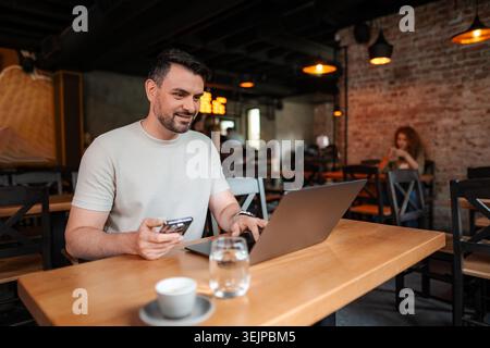 Young businessman using laptop and smartphone in a cafe Stock Photo