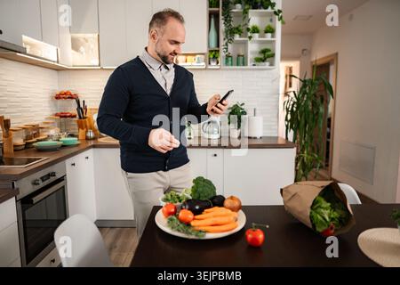 Man using smartphone checking ingredients in kitchen Stock Photo
