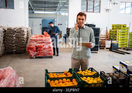 Two workers managing fresh produce inventory in a large distribution warehouse Stock Photo