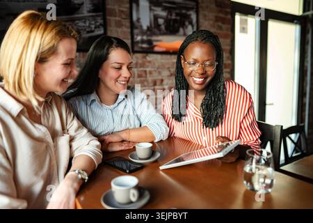 Diverse women friends smiling using digital tablet in cafe Stock Photo