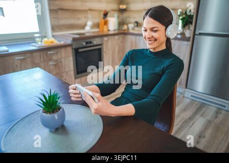 Young Woman Enjoying Music and Video Call in her Kitchen Stock Photo
