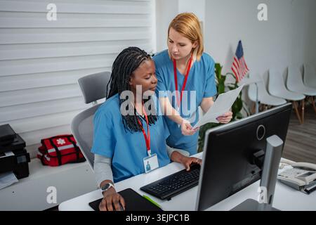 Two nurses collaborating on computer and paperwork at medical office Stock Photo