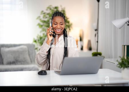 Happy young adult woman talking on phone working from home Stock Photo
