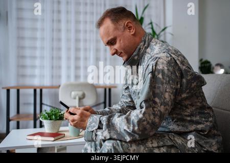 Soldier in camouflage uniform using smartphone at home Stock Photo