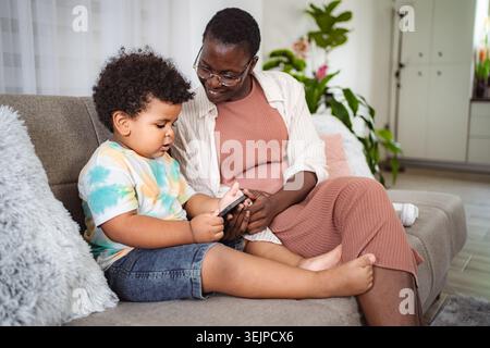 Mother and son using smartphone together on couch Stock Photo