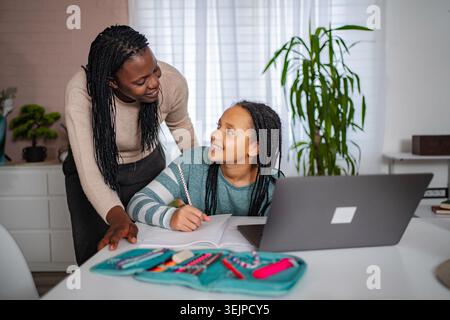 Mother helping daughter with homework using laptop at home Stock Photo