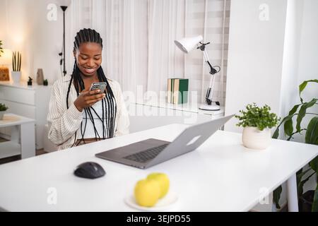 Young woman smiling using smartphone in home office Stock Photo