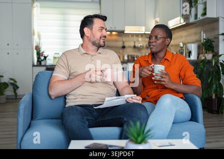 Couple relaxing on sofa, drinking coffee and discussing domestic bills Stock Photo