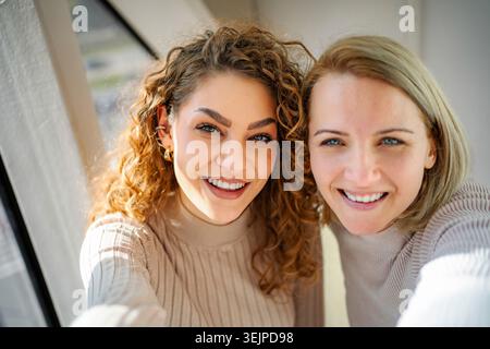 Two smiling women taking selfie indoors enjoying friendship Stock Photo