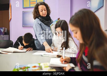 Female teacher helping elementary students at language school class Stock Photo